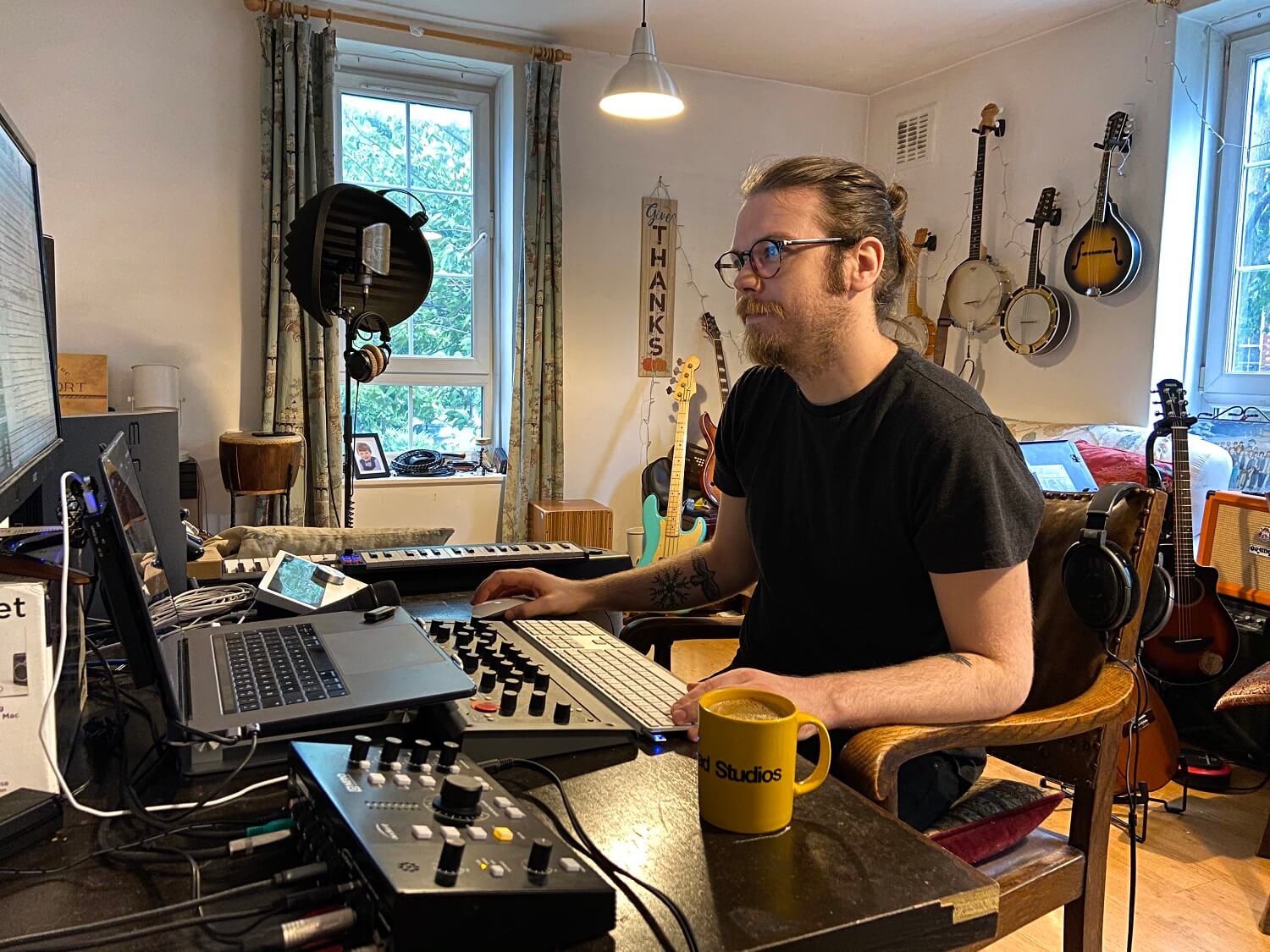 Man sits at desk with computer and lots of studio gear - and a cup of tea