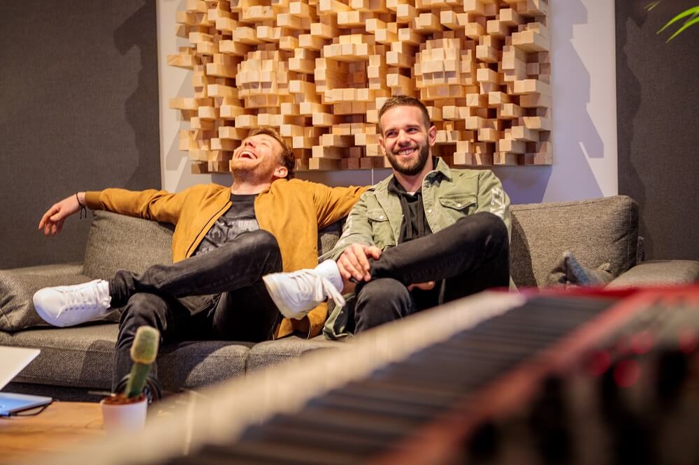 Two chaps laughing on a sofa (blurred piano keys in foreground)