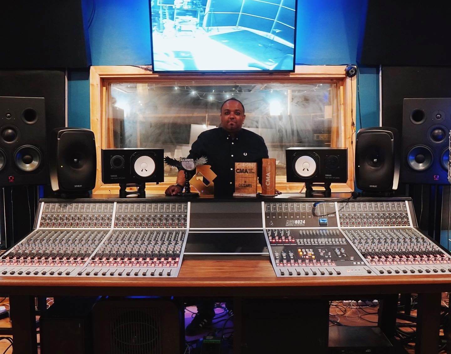 Man stands proudly behind a large format mixing console in his well-stocked studio