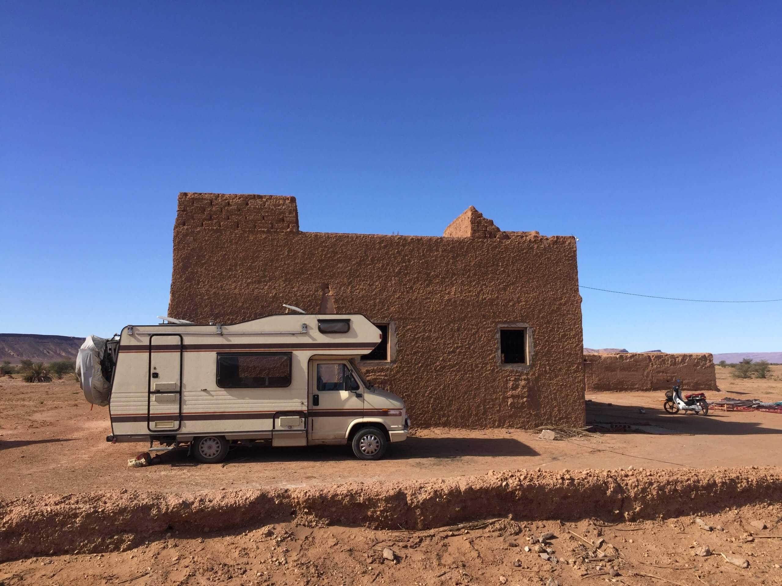 Campervan parked outside a sand building in a desert with bright blue sky