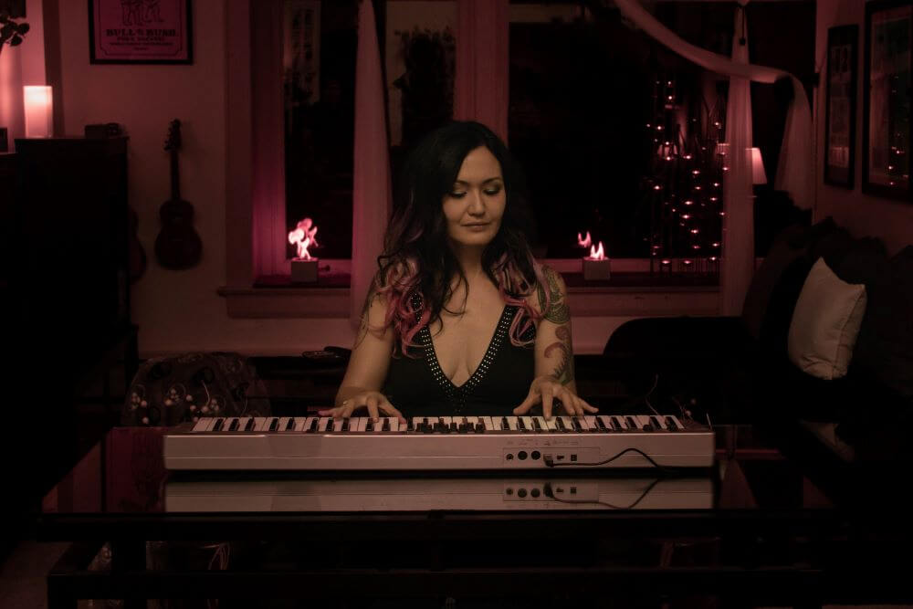 Elysha plays her keyboard in a home studio surrounded by twinkly lights 