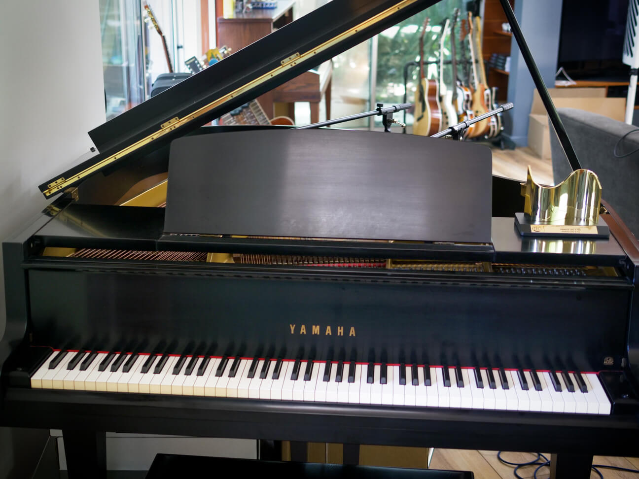 Lovely shiny Yamaha grand piano belonging to Warren Huart with an upright and at least five guitars in the background