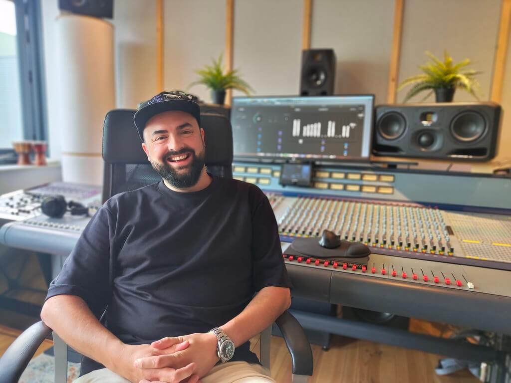 A relaxed-looking producer sitting with his back to a mixing console in a studio 