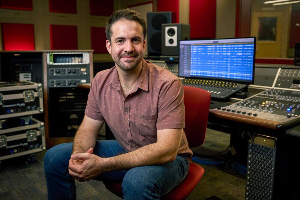 Approachable looking man sitting in front of Audient console in fully-stocked studio situation