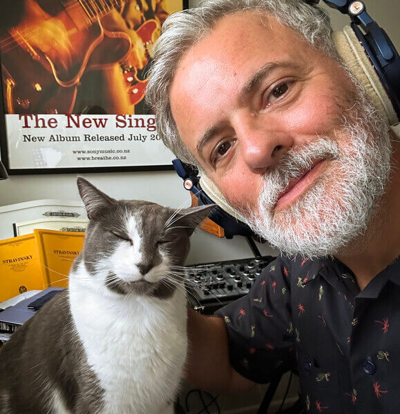 Grey & white contented cat sitting next to Stephen Gallagher wearing headphones 